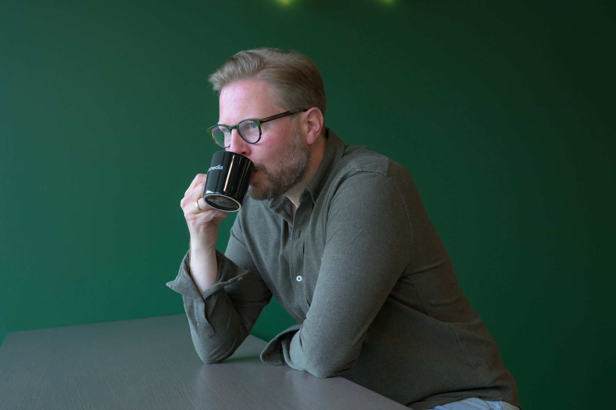 Mann drikker av kaffekopp med Amedia-logo