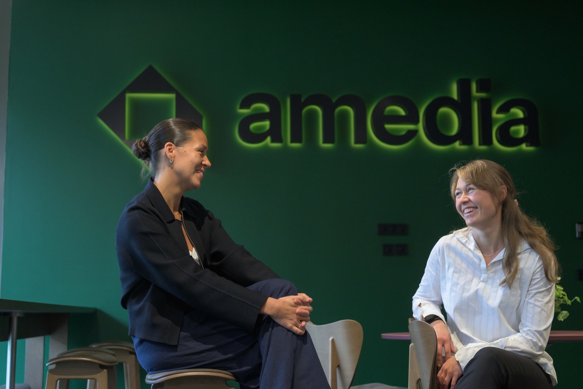 To kvinner med Amedia-logo i bakgrunnen