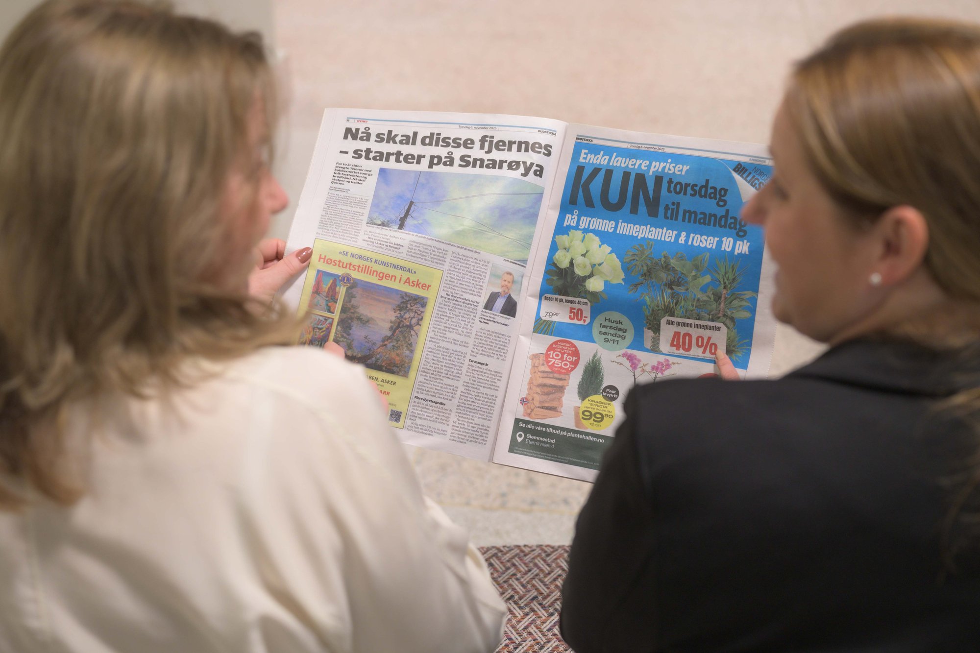 To kvinner ser på hverandre mens de leser papiravisa