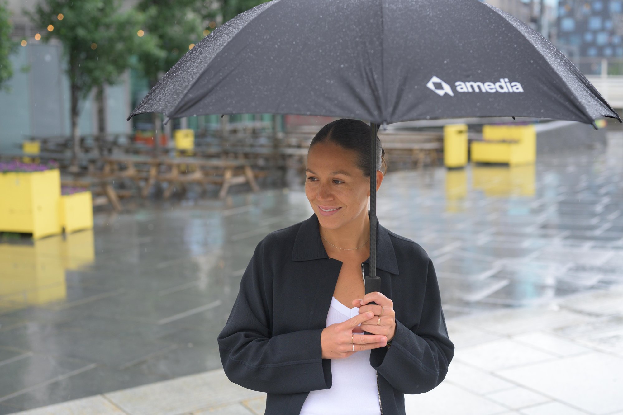 Smilende kvinne i regnet holder paraply