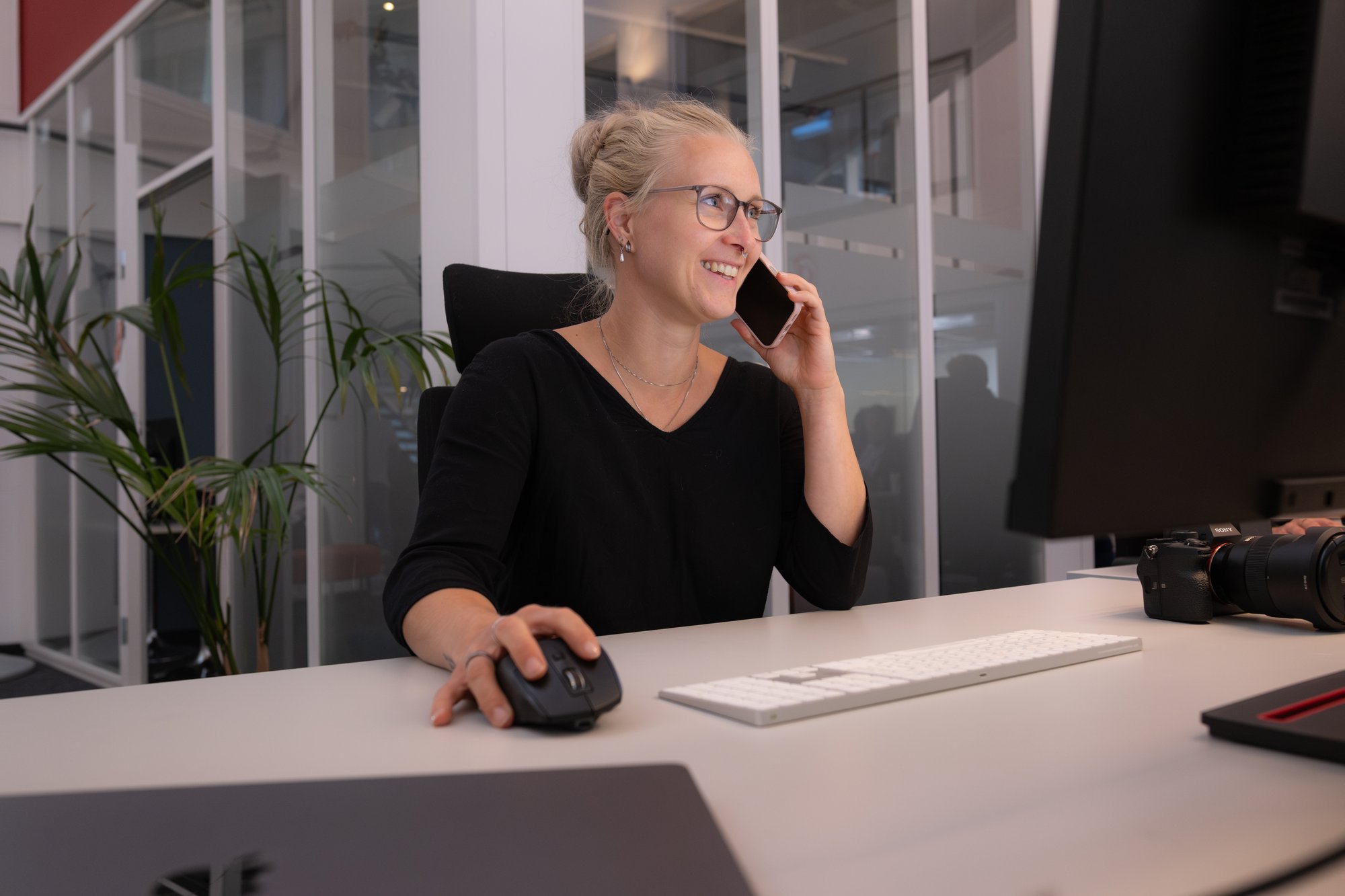 Smilende kvinne foran Mac med mobiltelefon - Amedia Annonse